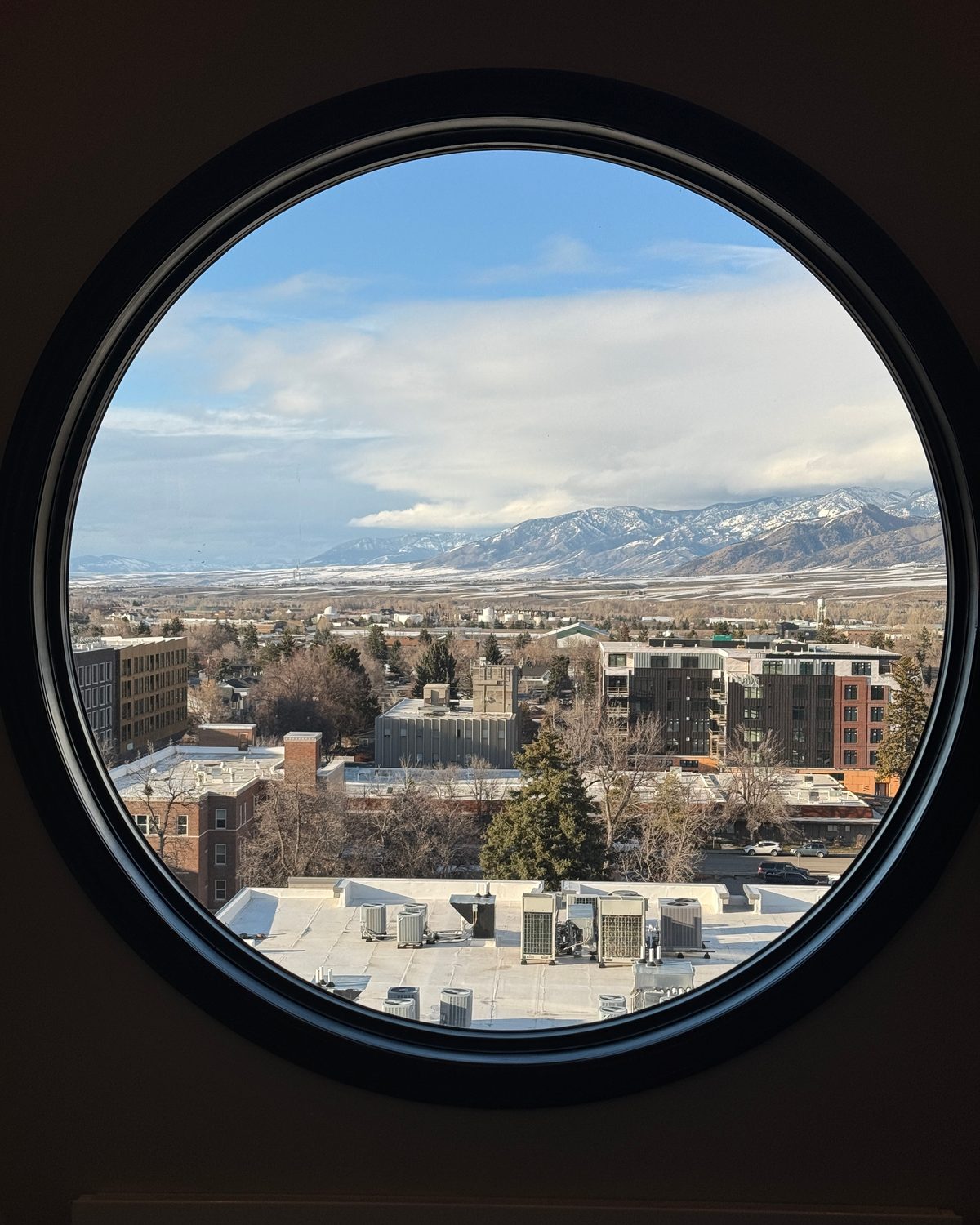 A round window framing a snow-capped skyline in Bozeman, Montana
